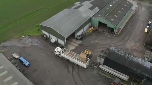 A pulling away aerial shot of a tractor loading up a truck full of corn in a farmyard in the country