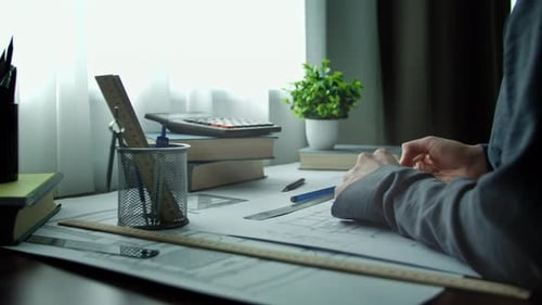 Architect Drawing at Wooden Desk with Tools and Books