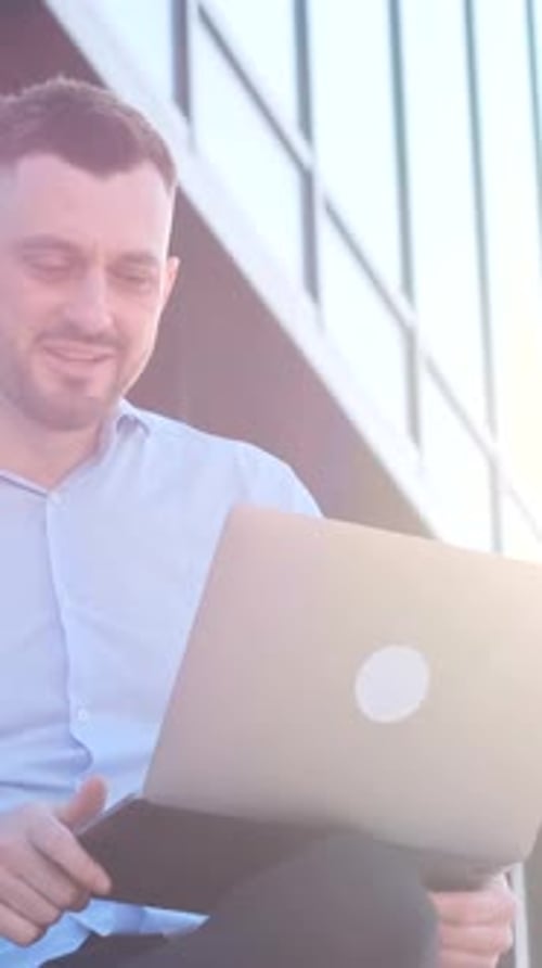 Handsome Bearded CFO Chatting Online on iPod Outdoors in Sunlight Against Glass Building Background