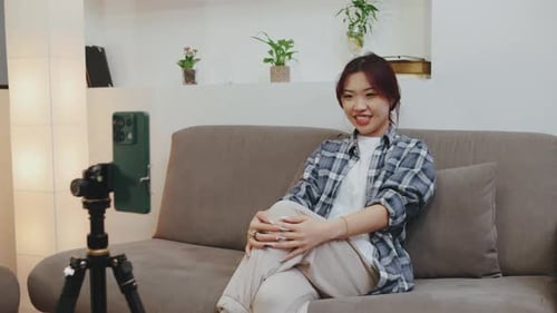 Young Woman Sits Comfortably on a Couch in a Welldecorated Indoor Area Engaging with Her Audience