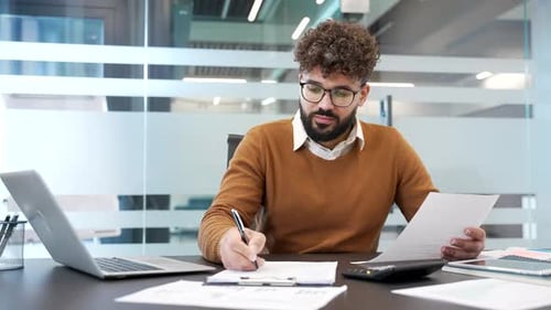 Busy businessman fills out documents with a pensitting at a work desk at workplace in modern glass