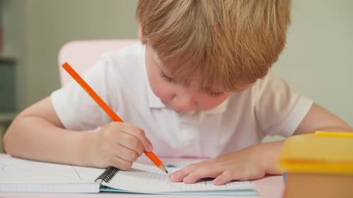 Child Drawing with Orange Pencil in Notebook