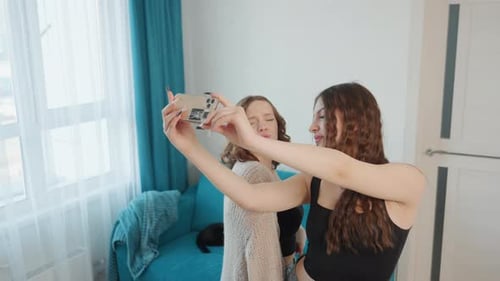 Two Smiling Women Taking a Selfie Indoors