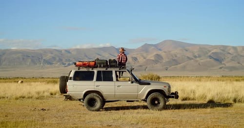 Traveler Stands Atop SUV in Remote Landscape