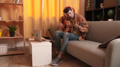Man Plays Guitar While Using Laptop at Home