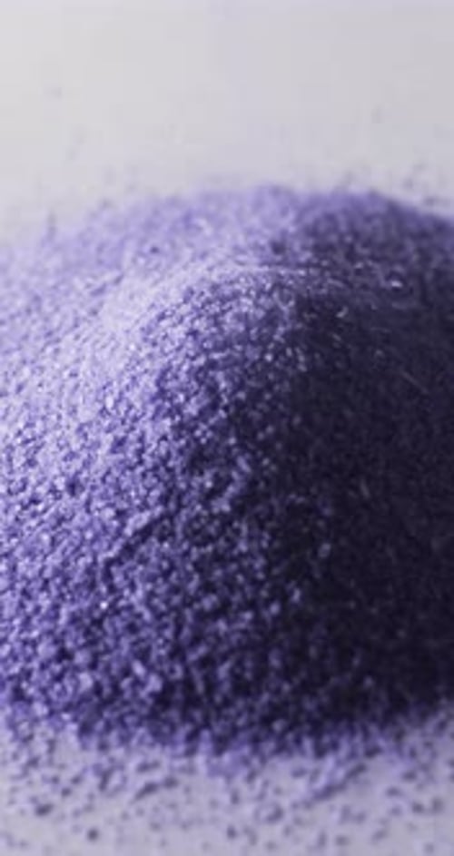 Vertical video of close up of heap of purple sand grains and copy space on white background