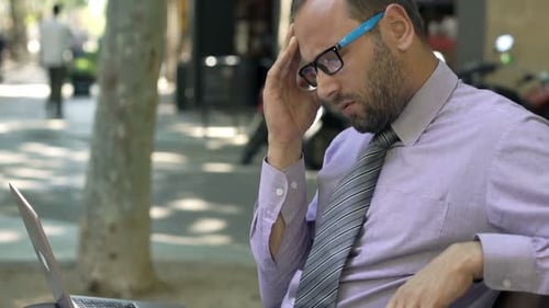 Businessman Having Head Pain Working on Laptop Sitting on Bench in City 30s