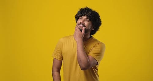 Pensive Young Indian Man Thinking with Hand Near Chin Standing Over Orange Studio Background