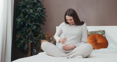 Pregnant Woman Sitting on Bed and Touching Stomach