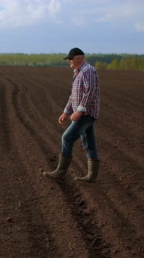 Farmer Walking Alone Across Freshly Plowed Agricultural Field at Sunrise Inspecting Soil Conditions