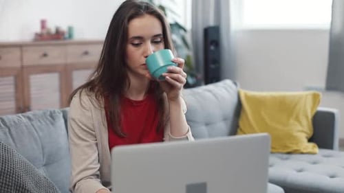 Woman Uses Laptop While Relaxing on Sofa