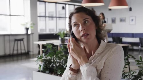 Caucasian casual businesswoman talking on smartphone in office, slow motion