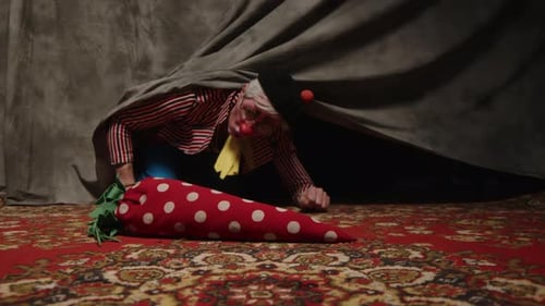 Clown Emerges with Polka-Dotted Carrot Under Gray Sheet