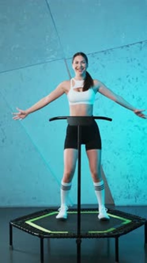 Joven enérgica chica de fitness con top blanco y pantalones cortos negros haciendo ejercicios saltando en el móvil mini tr