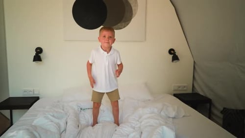 Happy Child Jumps on Bed in Bright Bedroom