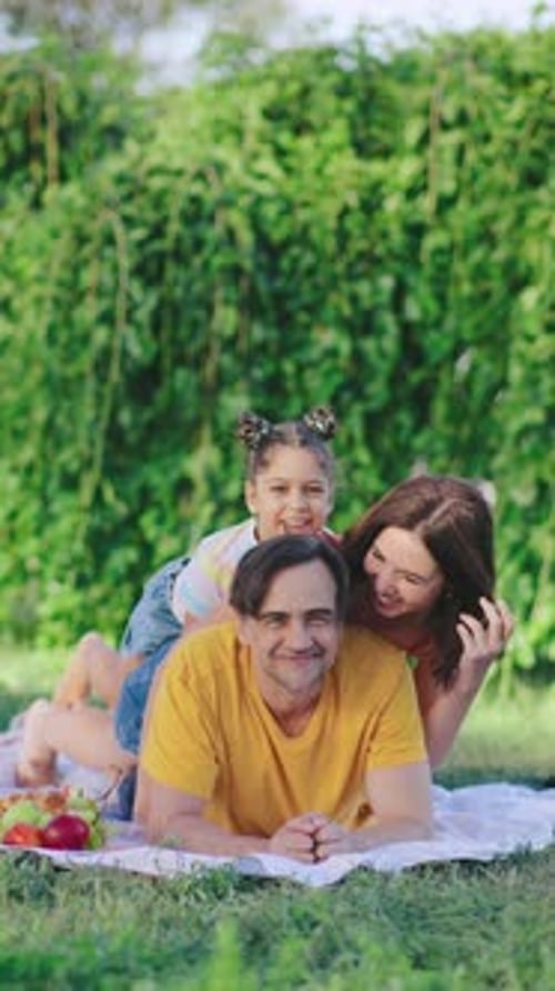 Family Enjoys a Sunny Picnic in a Park While a Child Playfully Rides on Her Parent's Back