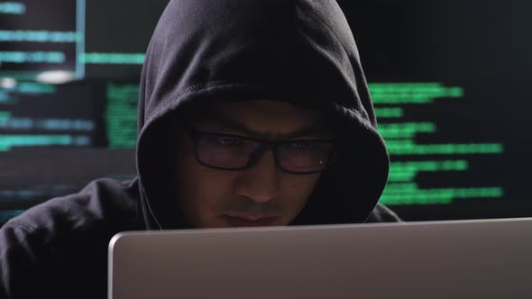 Vista de perto de um hacker asiático com capuz trabalha em um laptop ...