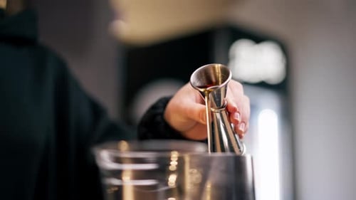 Eine Aufnahme der Bar hinter der Bar gießt Milch aus einem Messbecher in ein eisernes Milchkännchen