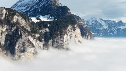 steep swiss cliffs rise from a drifting cloud ocean beneath broad snowy alpine slopes
