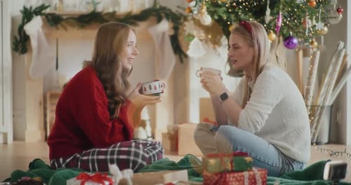 Hermosas hermanas hablando mientras sostienen tazas de café durante la Navidad en casa