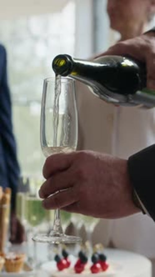 Vertical de homem irreconhecível derramando vinho espumante em copo na festa de negócios