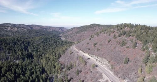 Autos fahren eine Straße auf einem Berg entlang, umgeben von Pinienwäldern, Drohnenantenne