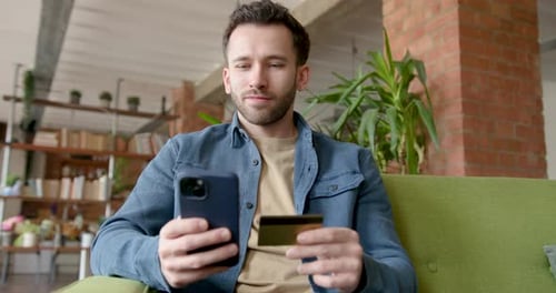 Man Uses Phone with Credit Card on Sofa