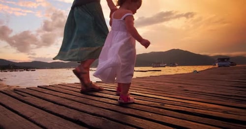 Familienspaziergang am Pier. Frau und Kleinkind gehen bei Sonnenuntergang auf dem Holzsteg
spazieren
