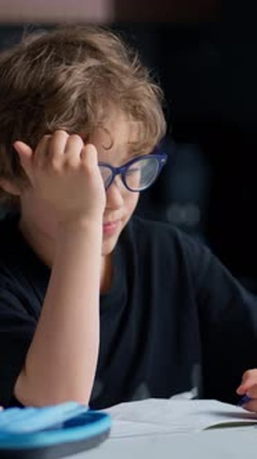Young Boy with Curly Hair Wearing Blue Glasses Focusing Intently While Reading and Studying at a