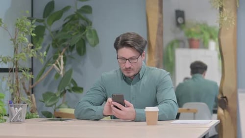 Middle Aged Man Browsing Internet on Smartphone in Office