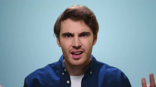 Displeased caucasian man gesturing annoyedly on blue background in slow motion studio
