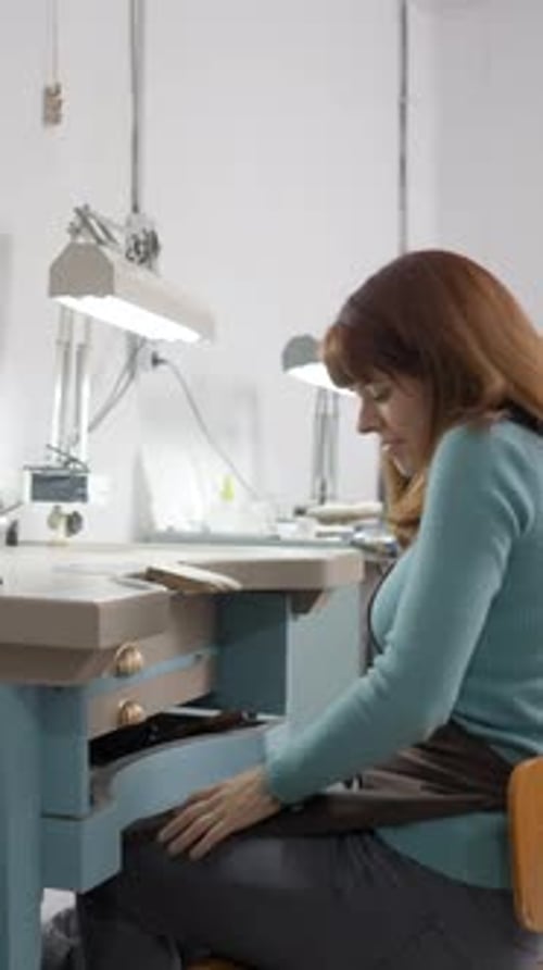 Young Freelance Jeweler With Apron Working On Table At Her Workshop Medium Shot