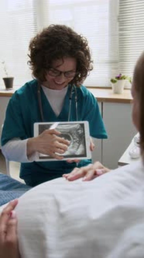 Cheerful Midwife Showing Baby Ultrasound to Pregnant Woman in Hospital