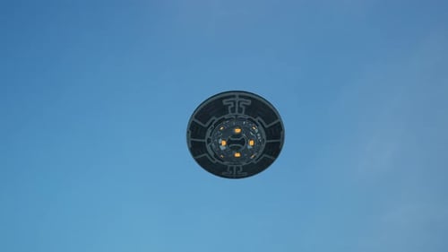 Tiefansicht einer kreisförmigen UFO-Untertasse, die in einem klaren blauen Himmel schwebt