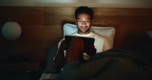 Man Relaxing and Watching Tablet in Bed at Night