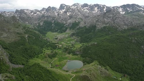 Flying over beautiful green mountains. In the background, stone cliffs with snow are visible.