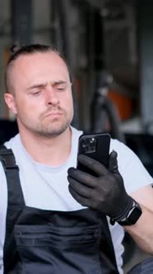 Vertical Video a Man on Garage Floor Phone in Hand Surrounded By Automotive Gear and Equipment