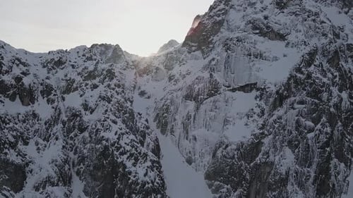 Drone footage of a sunrise above a snowy mountain cliff.