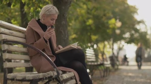 Woman Reading Book and Drinking Coffee on Bench