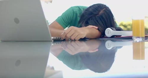 Teenage Asian boy rests his head on a desk at home while studying
