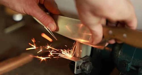 Man sharpening knife with bench grinder indoors, closeup
