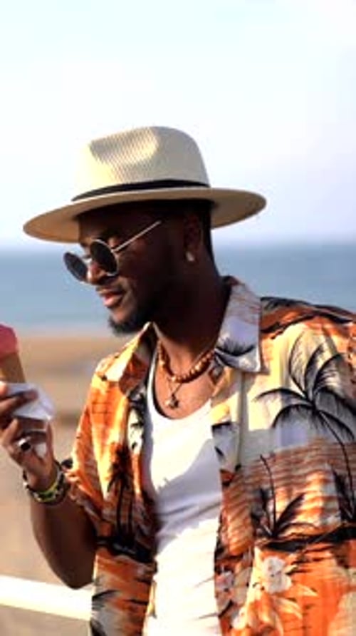 Black ethnic man enjoy summer vacation on the beach eating an ice cream enjoying strolling