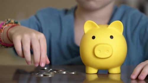 Kid Deposits Coin in Piggy Bank Child Carefully Drops Coin Into Bright Piggybank During Play