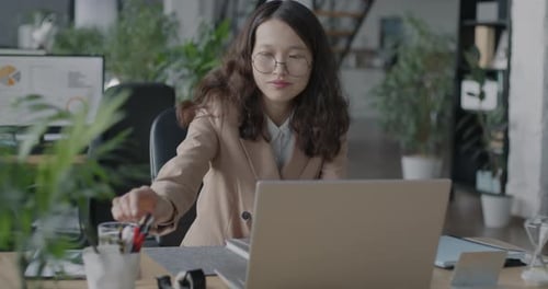 Slow Motion Portrait of Young Asian Lady Using Laptop Computer Sitting at Desk in Office Looking at