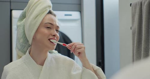 Mujer joven que sostiene un cepillo de dientes cepillándose los dientes mirándose en el espejo limpiándose la boca haciendo una oral matutina