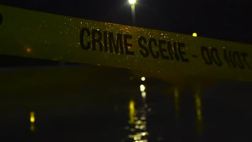Yellow crime scene tape in heavy rainfall during night time, covered with raindrops, street lights.