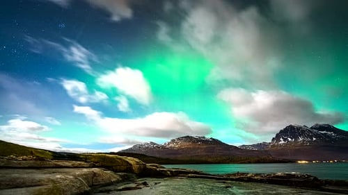 Northern lights flare in sky above flying clouds in Norway, motion time lapse