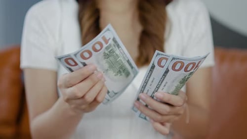 Close up hand girl counting money cash on sofa at home. Young woman planning budget income earnings.