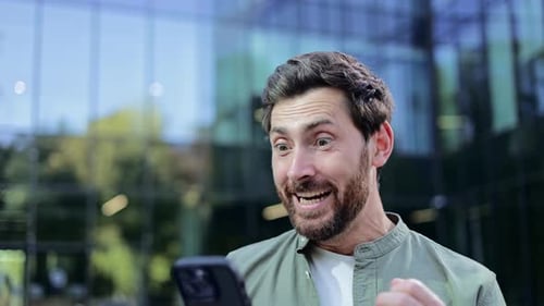 Man Cheers While Looking at Phone Outside Building