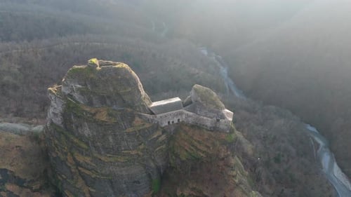 Ancient castle atop a rugged cliff with a river winding in the background at dusk, aerial view